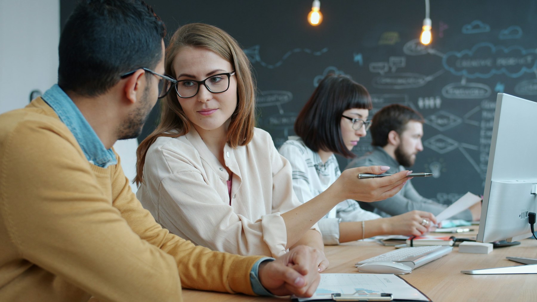 Equipe profissional colaborando diante de um computador em ambiente de trabalho moderno